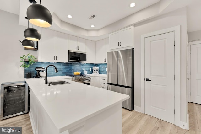 kitchen with a sink, stainless steel appliances, a peninsula, wine cooler, and visible vents