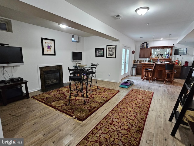 living area featuring visible vents, light wood-style floors, baseboards, a bar, and a fireplace with flush hearth