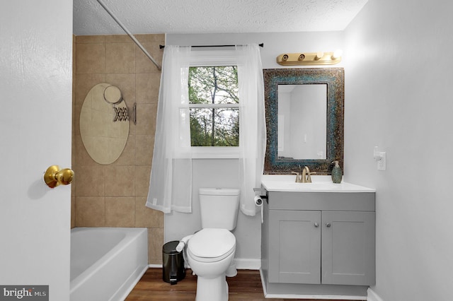 bathroom featuring vanity, wood finished floors, toilet, a textured ceiling, and shower / washtub combination