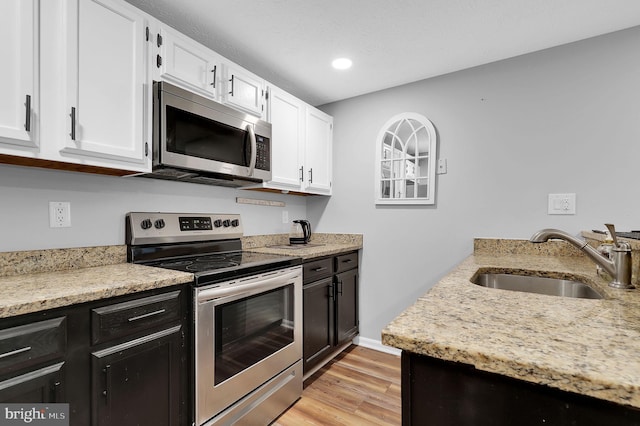 kitchen with light stone countertops, white cabinetry, a sink, light wood-style flooring, and appliances with stainless steel finishes