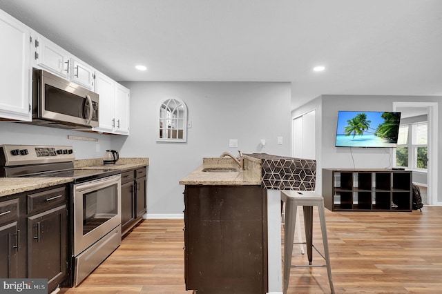 kitchen with a breakfast bar, light stone counters, a sink, stainless steel appliances, and recessed lighting