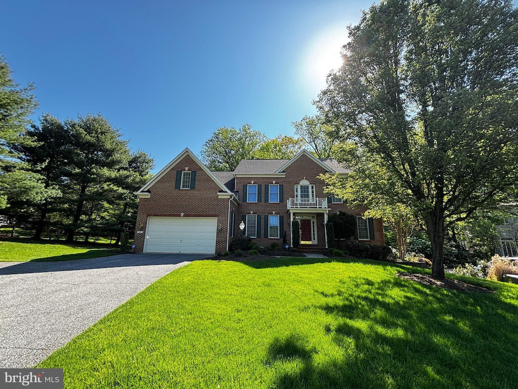 colonial-style house featuring an attached garage, a front yard, driveway, and brick siding