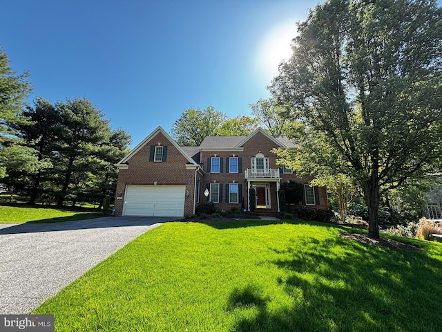 colonial-style house featuring an attached garage, a front yard, driveway, and brick siding