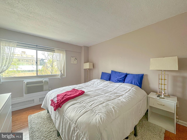 bedroom with baseboards, a wall unit AC, a textured ceiling, and wood finished floors