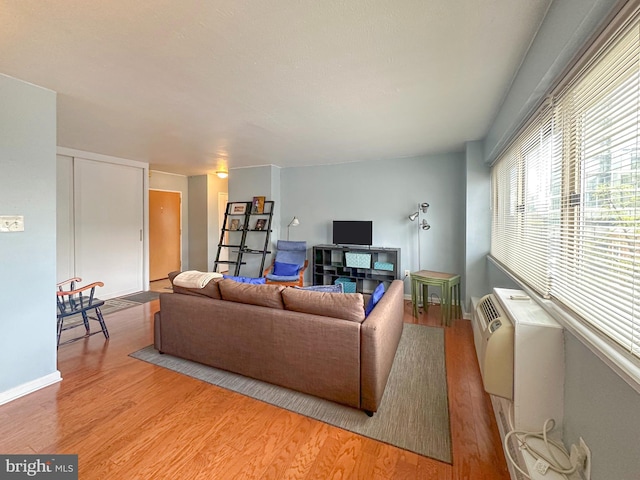 living room with baseboards, light wood-style flooring, and a wall mounted AC