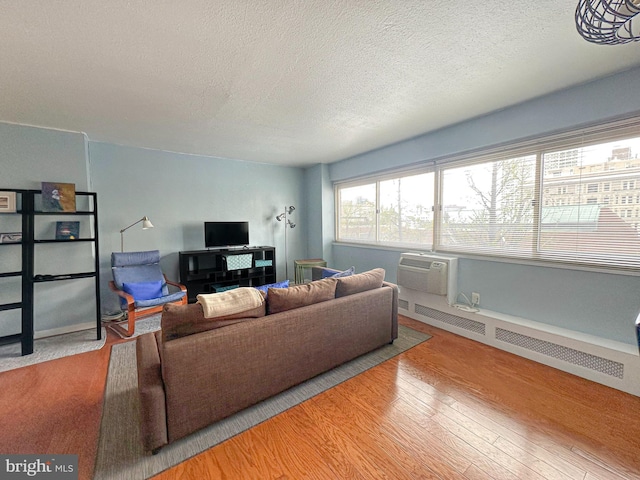 living room with a wall mounted air conditioner, a textured ceiling, wood finished floors, and baseboard heating