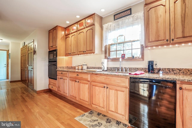 kitchen featuring light stone counters, a sink, black appliances, and light wood-type flooring