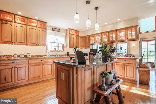 kitchen featuring dark stone countertops, glass insert cabinets, light wood-style flooring, and a center island