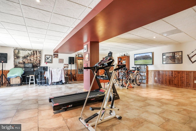 workout room featuring wood walls, a paneled ceiling, and a wainscoted wall