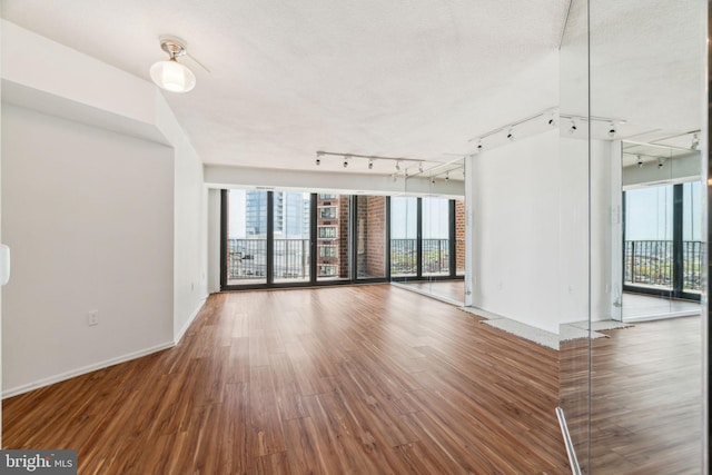 unfurnished living room featuring track lighting, baseboards, and wood finished floors