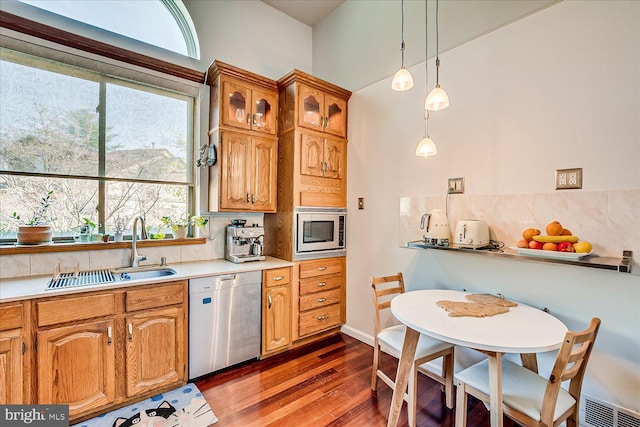 kitchen featuring stainless steel appliances, backsplash, light countertops, wood finished floors, and a sink