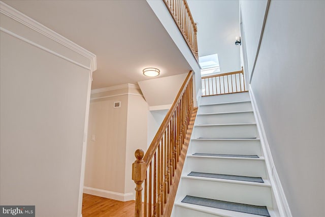 staircase featuring wood finished floors, visible vents, a skylight, crown molding, and baseboards