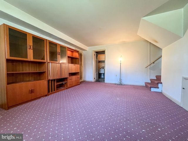 unfurnished living room featuring carpet floors, baseboards, and stairs