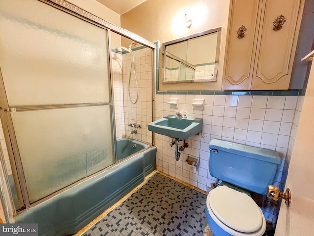 bathroom featuring toilet, tile walls, and combined bath / shower with glass door