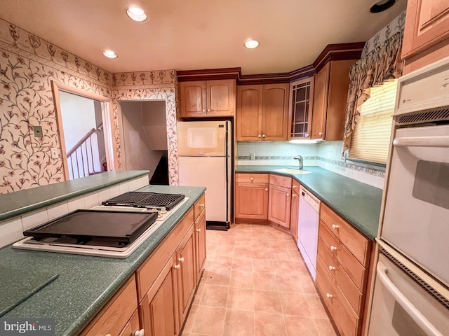 kitchen with a sink, recessed lighting, glass insert cabinets, wallpapered walls, and white appliances
