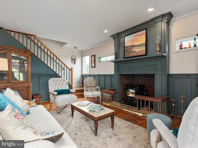 living room with wood finished floors, crown molding, a decorative wall, a wood stove, and stairs
