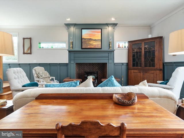 living room with a large fireplace, crown molding, a decorative wall, and wainscoting