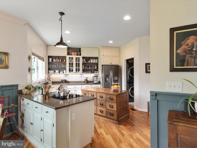 kitchen with open shelves, light wood finished floors, stainless steel fridge, black stovetop, and stacked washing maching and dryer