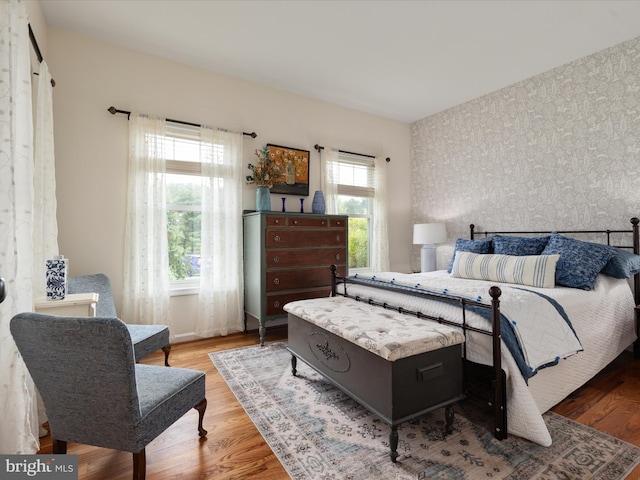 bedroom featuring an accent wall, wallpapered walls, and wood finished floors