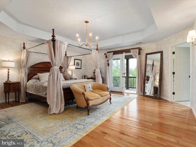 bedroom with a tray ceiling, light wood-style floors, access to exterior, and a notable chandelier
