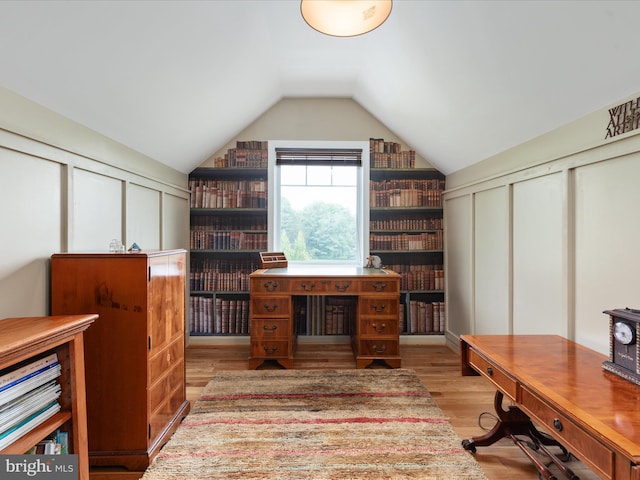 office area with a decorative wall, wood finished floors, and vaulted ceiling