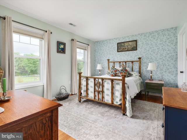 bedroom with visible vents, wallpapered walls, and wood finished floors