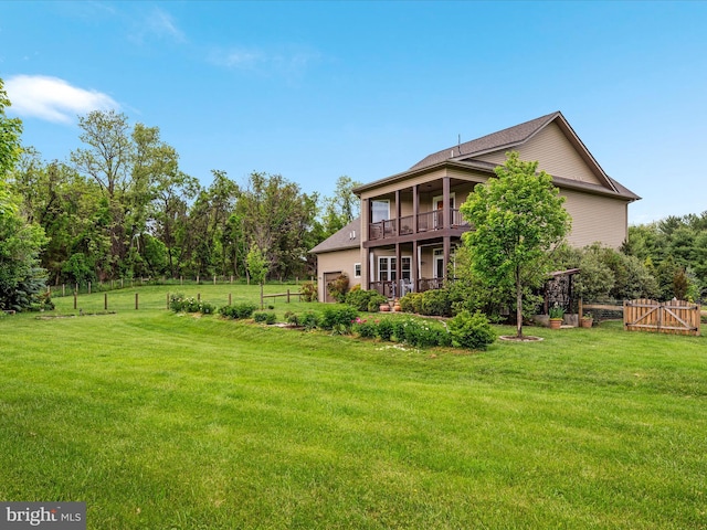 rear view of property with a lawn, a balcony, and fence