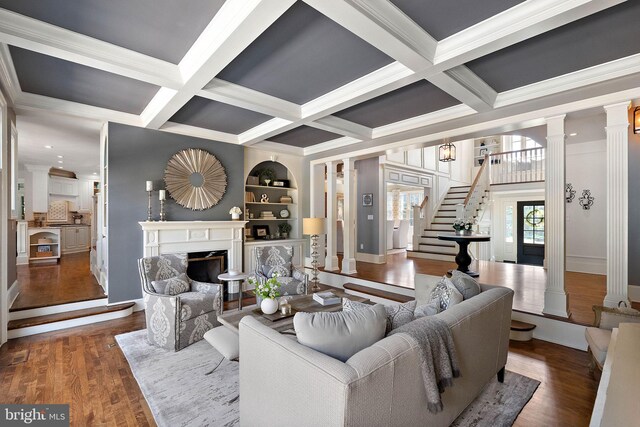 living room with ornate columns, coffered ceiling, a high end fireplace, wood finished floors, and stairs