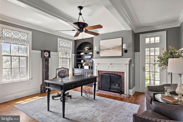 office featuring a decorative wall, a brick fireplace, plenty of natural light, wood finished floors, and a ceiling fan