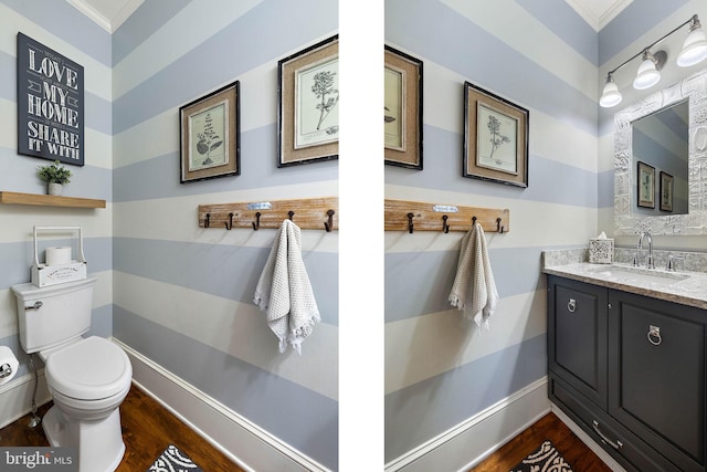 half bath with crown molding, wood finished floors, toilet, vanity, and baseboards