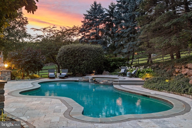 pool at dusk with a patio area and a pool with connected hot tub