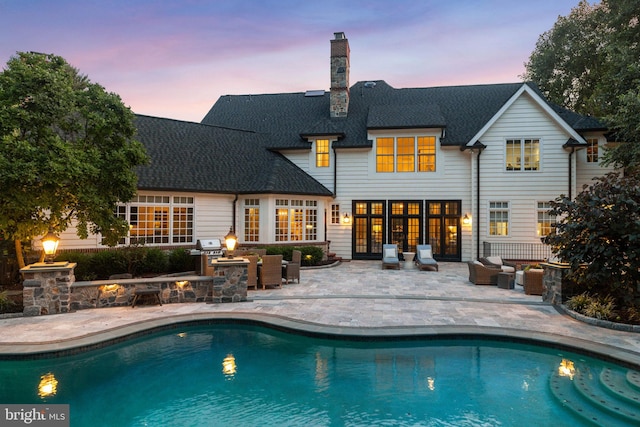 back of property with a patio, an outdoor pool, a chimney, and french doors