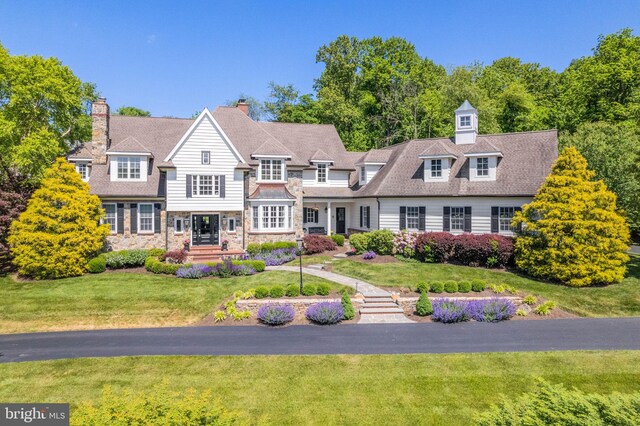 shingle-style home featuring a front lawn, stone siding, and a chimney