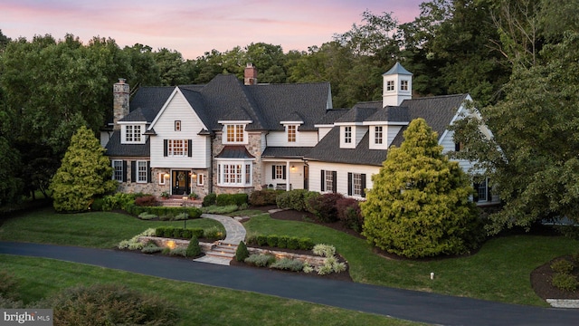 shingle-style home with a front yard, a chimney, and stone siding