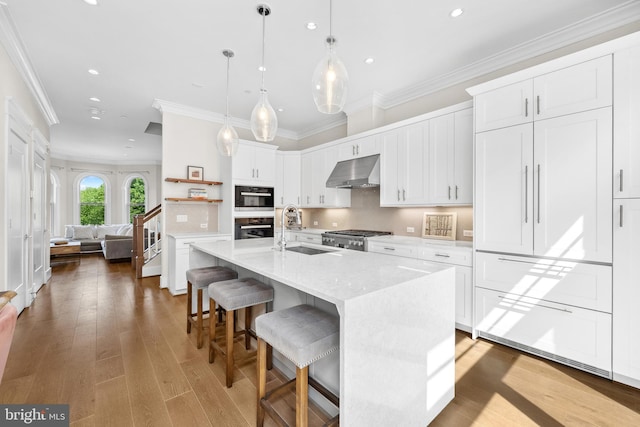 kitchen with recessed lighting, under cabinet range hood, crown molding, and a sink