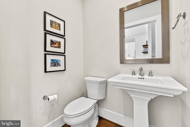 half bathroom with a sink, toilet, and baseboards