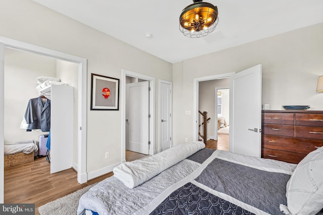 bedroom with wood finished floors, a closet, a walk in closet, and baseboards