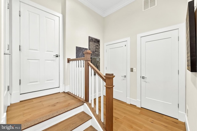 foyer entrance with visible vents, crown molding, and light wood finished floors