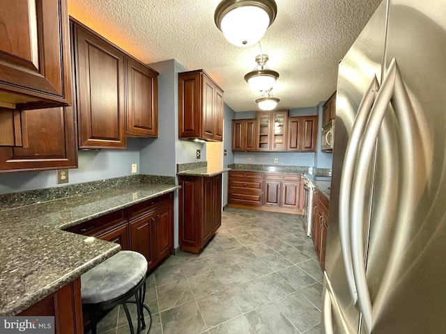 kitchen with glass insert cabinets, a textured ceiling, dark stone counters, and stainless steel appliances