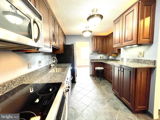 kitchen featuring light stone counters, electric stove, a sink, stainless steel microwave, and glass insert cabinets