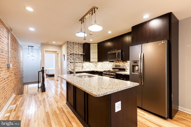 kitchen with open shelves, appliances with stainless steel finishes, a sink, brick wall, and light wood-style flooring