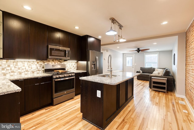 kitchen featuring decorative backsplash, decorative light fixtures, appliances with stainless steel finishes, a sink, and light wood-style flooring