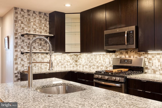 kitchen with a sink, light stone counters, dark brown cabinetry, and stainless steel appliances