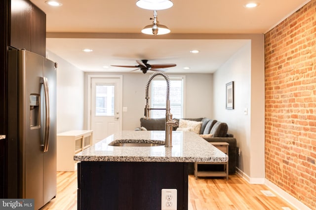 kitchen with stainless steel refrigerator with ice dispenser, a sink, light wood-style floors, and brick wall