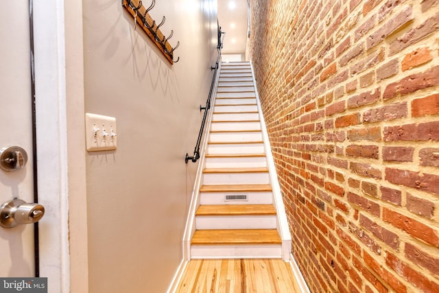 stairway featuring wood finished floors and brick wall