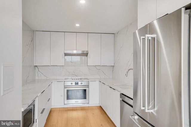 kitchen featuring white cabinets, under cabinet range hood, modern cabinets, a sink, and appliances with stainless steel finishes