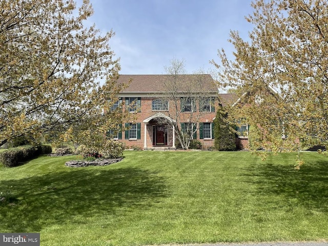 colonial house featuring brick siding, a shingled roof, and a front lawn