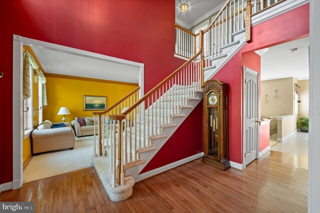stairway with crown molding, baseboards, a high ceiling, and hardwood / wood-style flooring