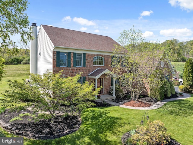colonial-style house with brick siding, a chimney, a front yard, and roof with shingles