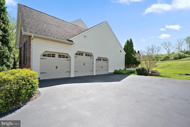 view of side of property featuring a garage, a shingled roof, and driveway